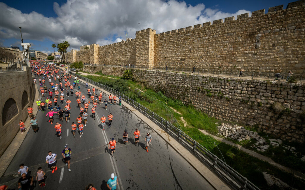 Runners in Jerusalem marathon 2024 next to old wall